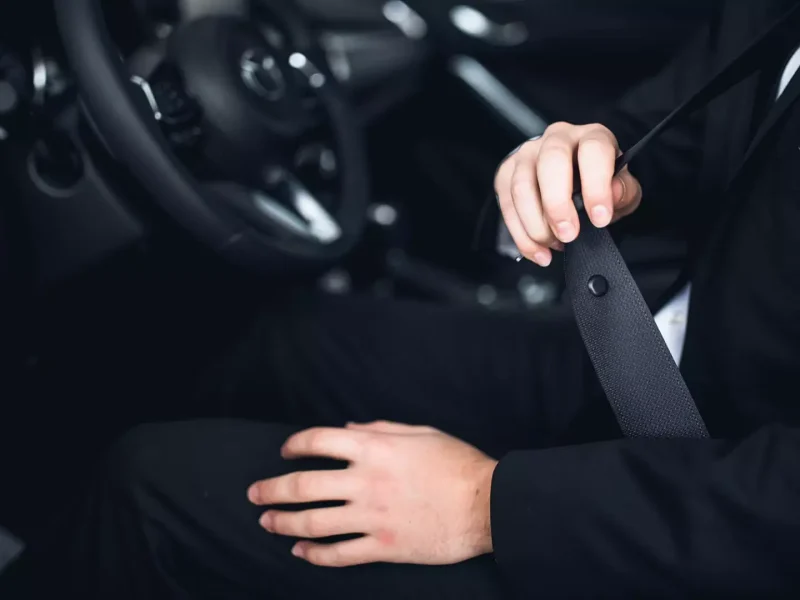 close up of the inside of a car, driving wheel and person putting the seatbelt